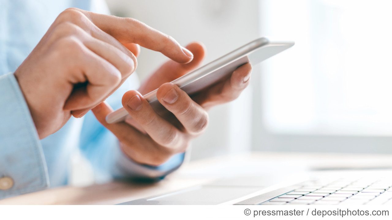 Hand hält Smartphone über einer Laptoptastatur und tippt auf den Screen