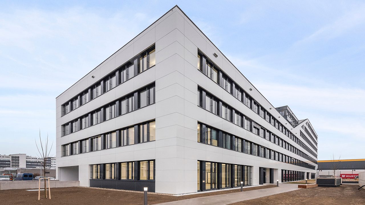 Außenansicht eines dreistöckien Bürogebäudes, neu gepflanzter Baum vor dem Haus