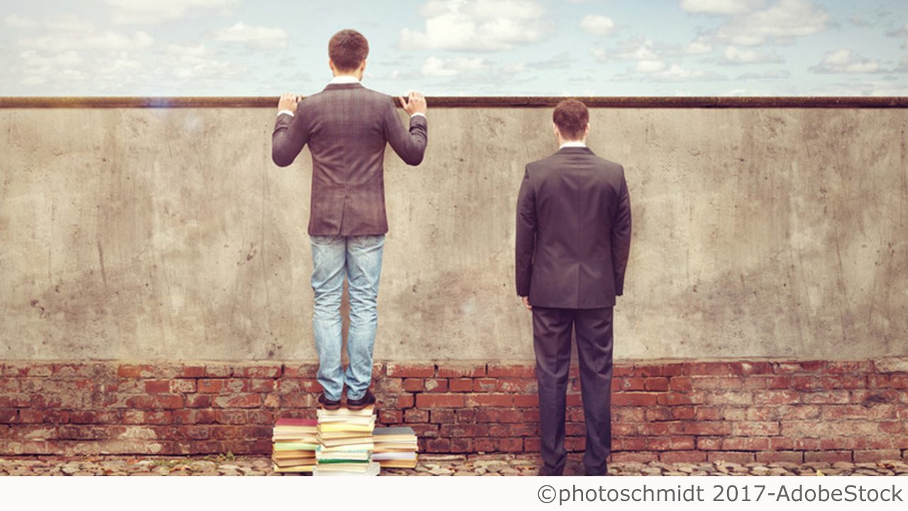 Zwei Personen stehen vor einer Mauer, einer steht auf einem Stapel Bücher und blickt über die Mauer, der andere starrt direkt in die Mauer