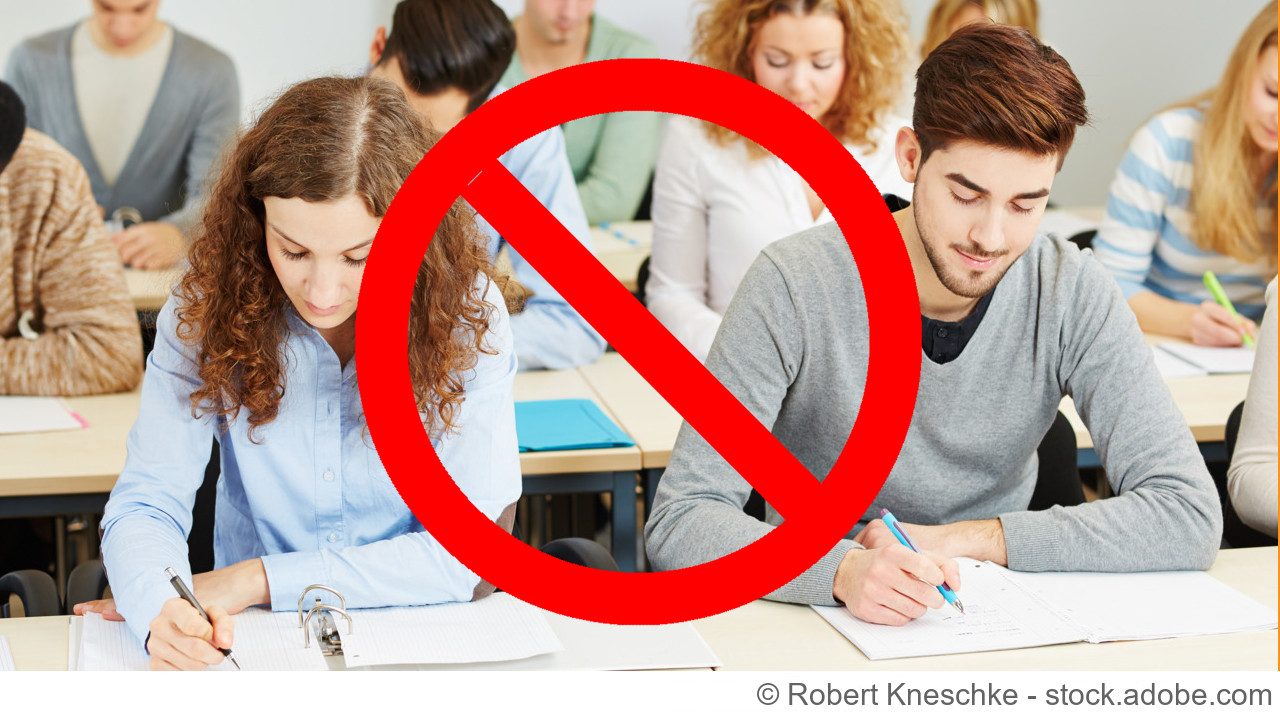 Gruppe von jungen erwachsenen lernenden / studierenden die in einem Klassenraum an Schreibtischen sitzen und in ihre Unterlagen schauen und schreiben