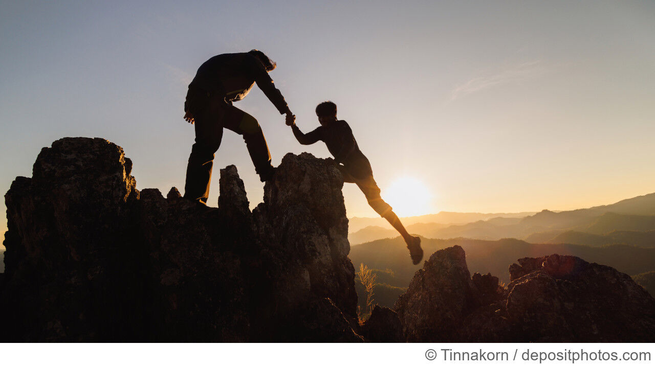2 Bergsteiger_innen erklimmen einen Felsen vor der untergehenden Sonne