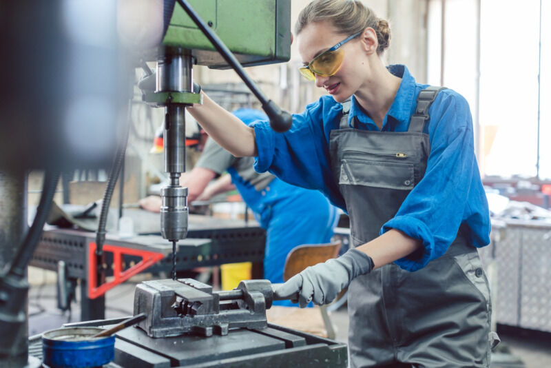 Metal worker woman operating drilling machine concentrating on her job