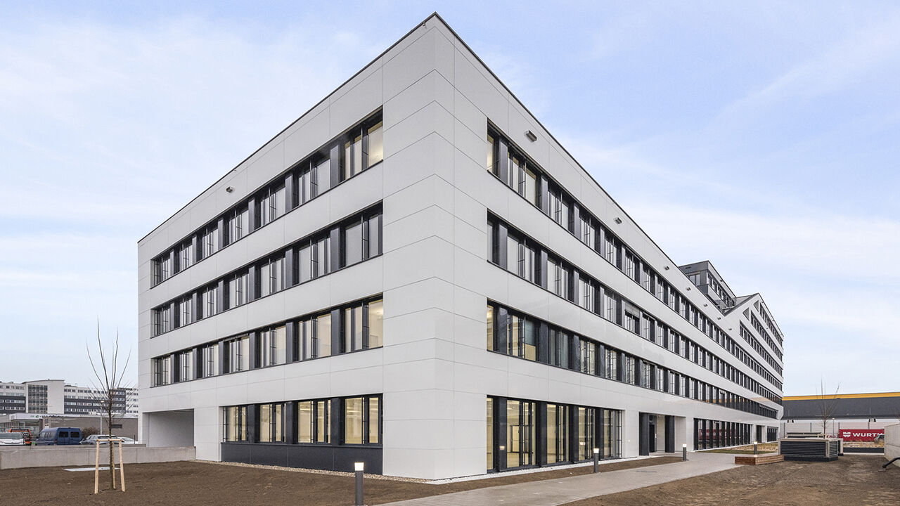 Außenansicht eines dreistöckien Bürogebäudes, neu gepflanzter Baum vor dem Haus